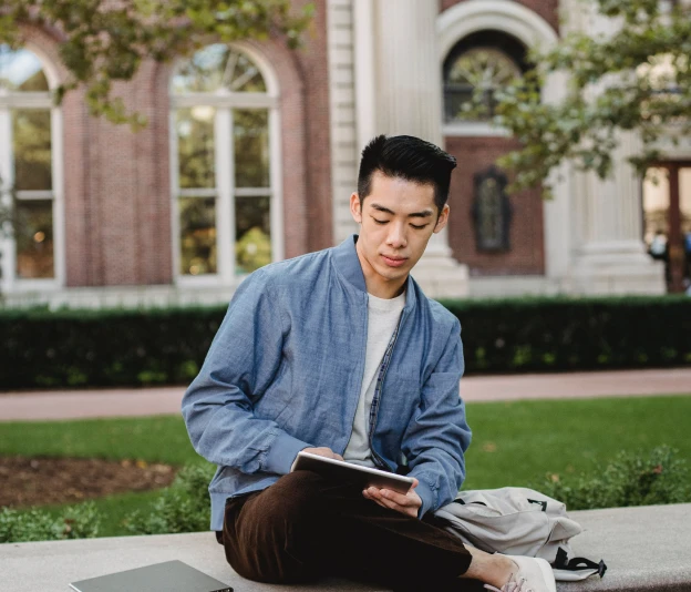 University student sitting on a bench and reading from tablet.